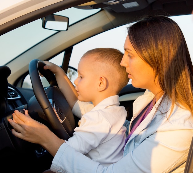 Мать и сын сидят за рулем автомобиля с руками ребенка за руль, как будто за рулем
