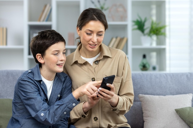 Mother and son sitting together on sofa at home in living room family looking at phone screen