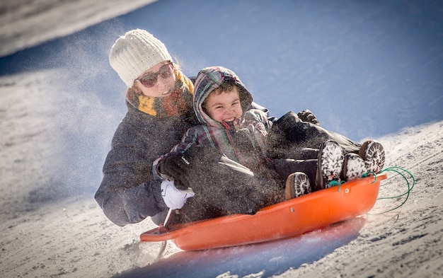 Photo mother and son sledding in the snow