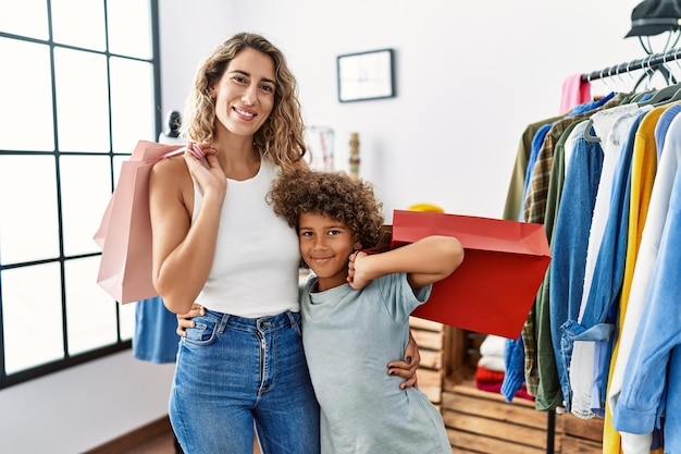 母と息子が自信を持って微笑み、抱き合い、衣料品店で買い物袋を持っている