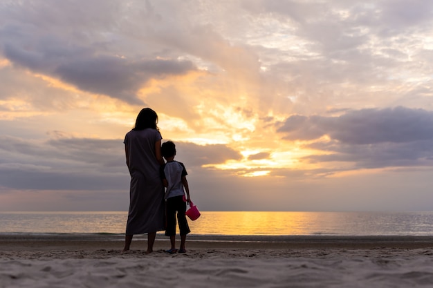 Mother and son standing on the beach watching sunset