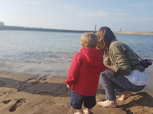 Photo mother and son standing on shore at beach