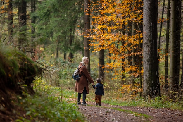 Photo mother and son walk through the forest in autumn