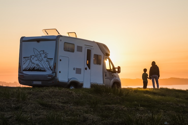 Photo mother and son watching the sunset with their motor home at the edge of the sea