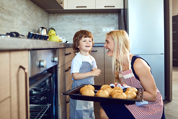 Photo mother and son with a tray of leaves from the oven in the kitchen.