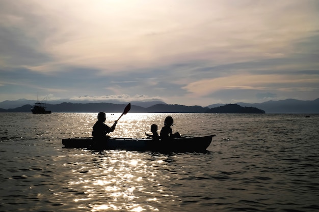 母と息子の休暇の背景に海でカヤックを漕ぐことは大きな山と夕日です。