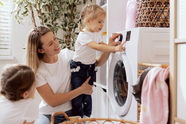 Mother spends time with young children in laundry room bathroom performs household duties