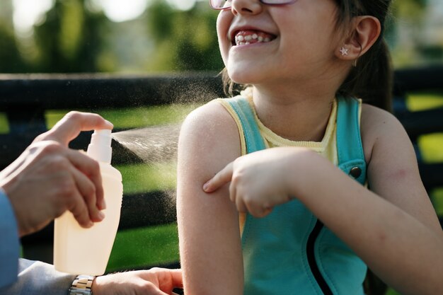 Mother spraying insect repellents on her daughter's skin.