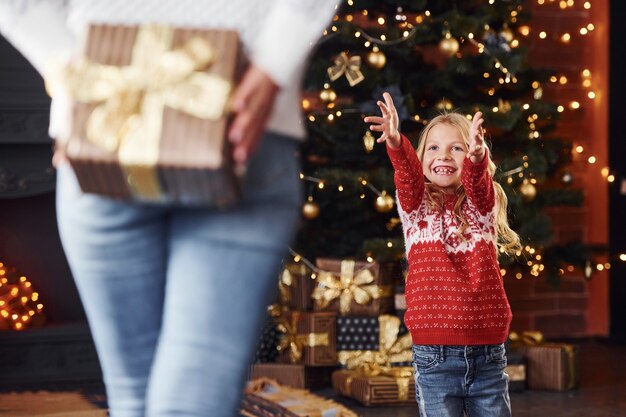 Фото Мать стоит с подарочной коробкой и делает сюрприз для дочери в помещении во время рождественских каникул.