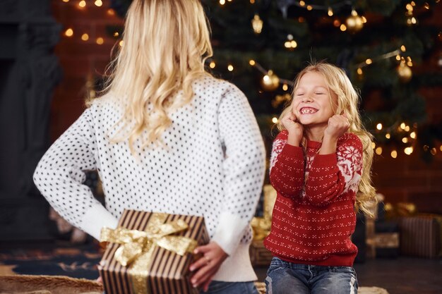 Mother standing with gift box and makes surprise for daughter indoors at christmas holidays time.