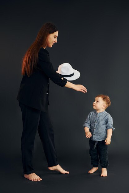 スタイリッシュな黒い服を着た母親は、スタジオで彼女の幼い息子と一緒にいます