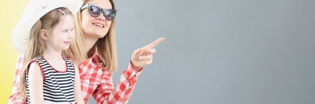 Mother in sunglasses showing her finger to little girl in hat