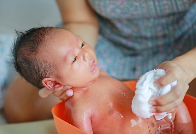 Mother taking a bath to her newborn baby in a bathtub.