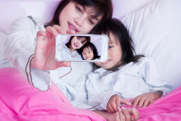 Mother taking selfie with daughter on bed at home