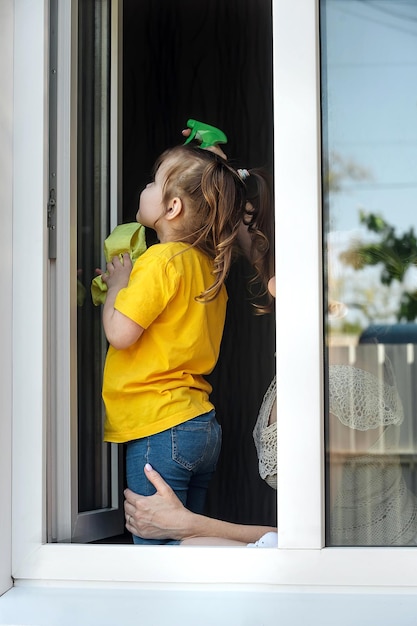 Mother teaches her daughter to clean the house, they clean the\
window together