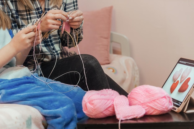 mother teaches her daughter to knit, in front of them is a tablet with a training video