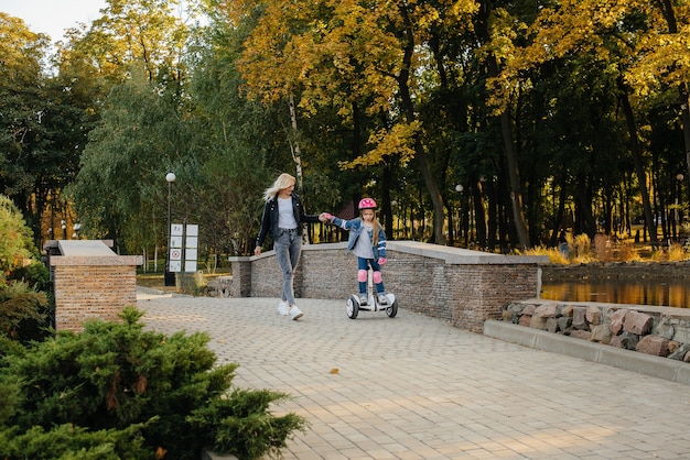 A mother teaches her little daughter to ride a Segway in the Park during sunset. Happy family vacation.