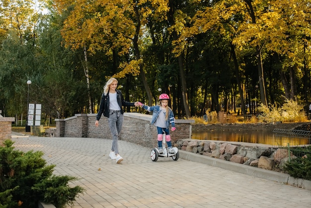 A mother teaches her little daughter to ride a Segway in the Park during sunset. Happy family vacation.