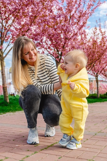 Mother teaching baby to walk surrounded by cherry blossoms