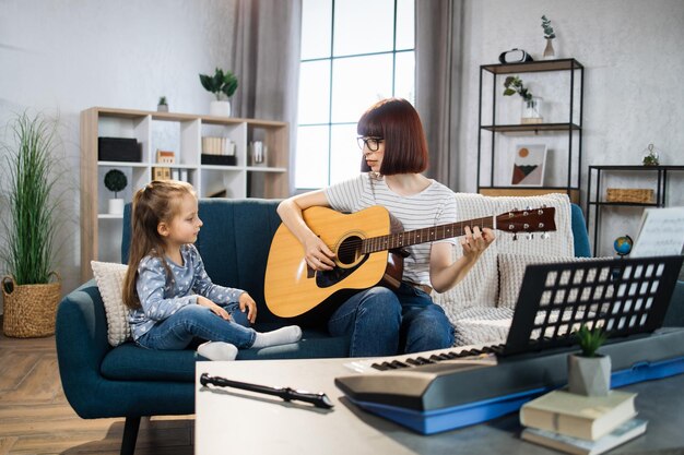 写真 かわいいミュージシャンの女の子にギターを弾くように教える母