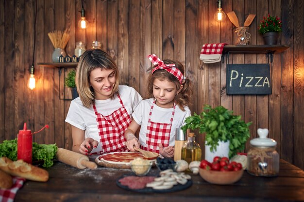 Mother teaching daughter cooking pizza and smiling