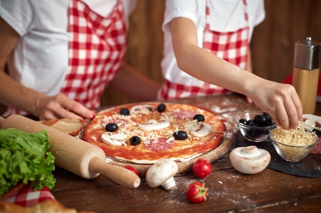 Mother teaching daughter cooking pizza and smiling