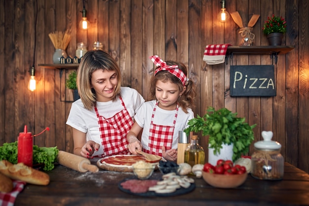 Mother teaching daughter cooking pizza and smiling