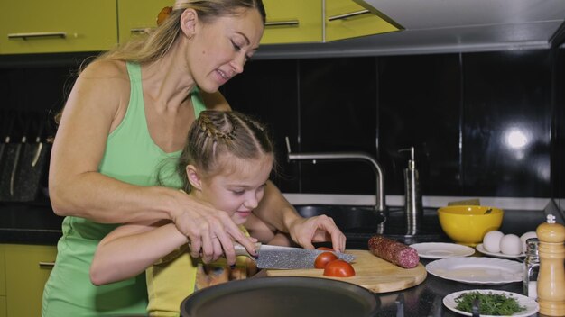 Mother teaching daughter smart girl learning to cook Mistress children to cook a Neapolitan egg fried omelette from salame affumicato sausage