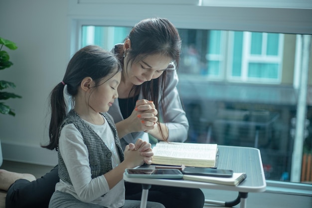 Mother teaching her daughter to praying and reading bible