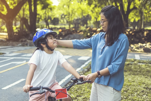 母は娘に公園で自転車に乗るように教えています。自転車に乗って屋外の家族。