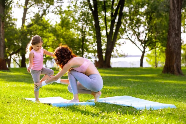 Mother teaching her daughter yoga in the park using yoga mat