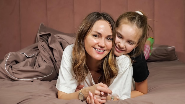 Photo mother and teen daughter have fun lying on bed at home
