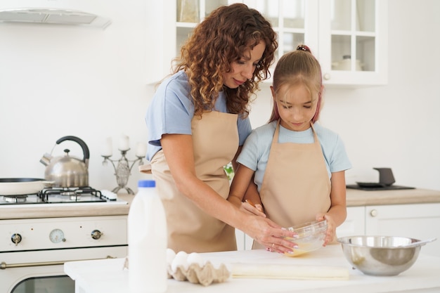 Mother and teen daughter making dough for pastry toghether in kitchen