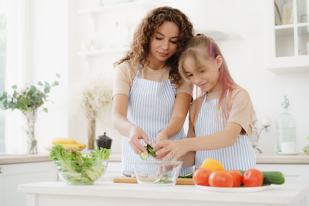 Mother and teen daughter preparing vegetable salad at kitchen