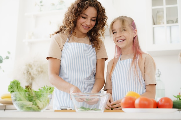 Mother and teen daughter preparing vegetable salad at kitchen