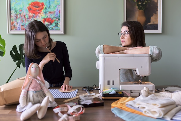 Mother and teen daughter sew together at home. Mom teaching daughter sewing on machine, women sew toy and clothes for toy. Parent and teenager, relationships, lifestyle, creativity, skill