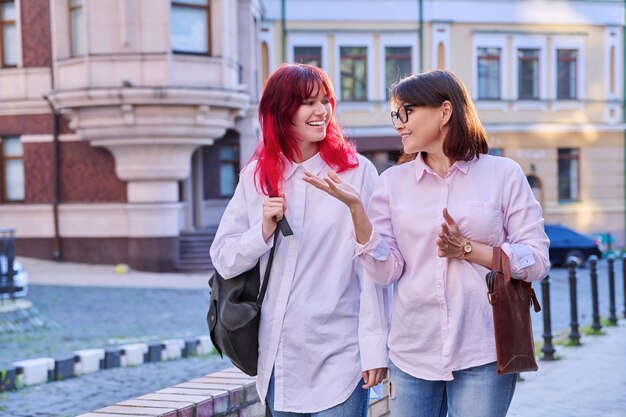 Mother and teenage daughter walking talking together along city street