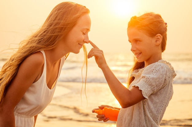 Mother and teenager daughter using sunscreen on the beach.