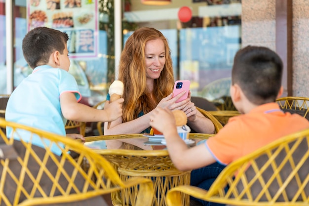 Mother on a terrace of a coffee shop with her two children looking her phone