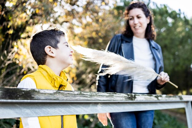 Foto madre che fa il solletico al figlio con una piuma sulla ringhiera nel parco