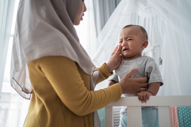 Mother try to comfort her cry child at the crib