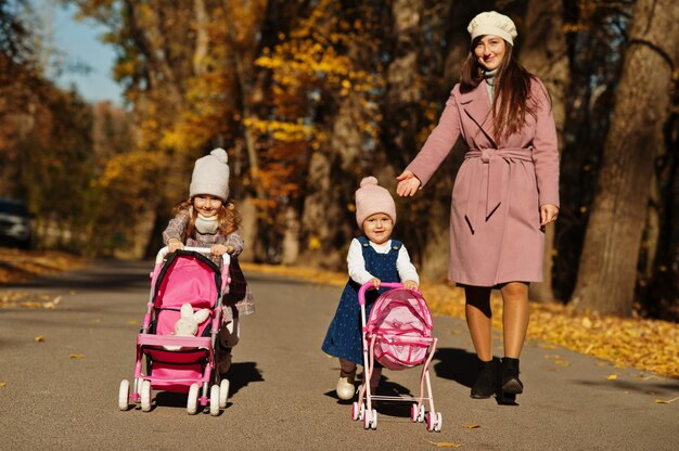 Mother and two baby daughters with stroller walking on autumn park.