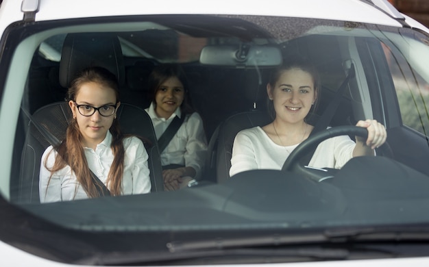 Mother and two daughters in school uniform riding in car