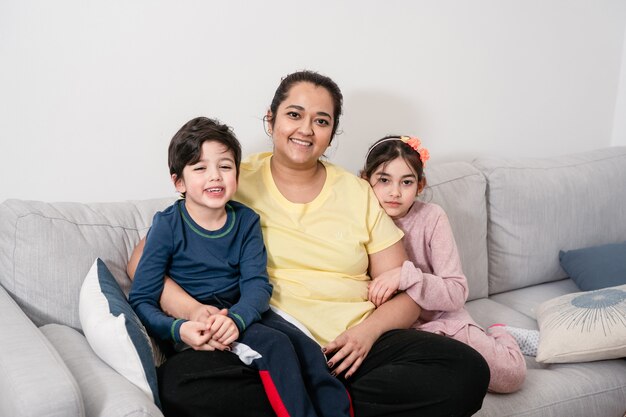 Madre e due bambini seduti sul divano sorridendo e guardando la fotocamera. persone di razza mista. vita reale, unione, diversità