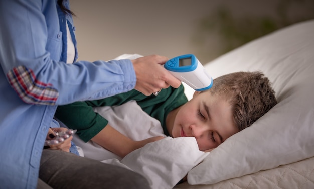 Photo mother uses thermometer to measure temperature of her sleeping boy in bed.