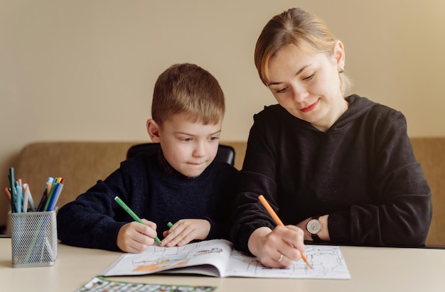 Mother using laptop and tablet teaching with her son online at\
home in his room