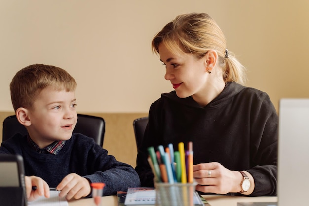 Mother using laptop and tablet teaching with her son online at home in his room