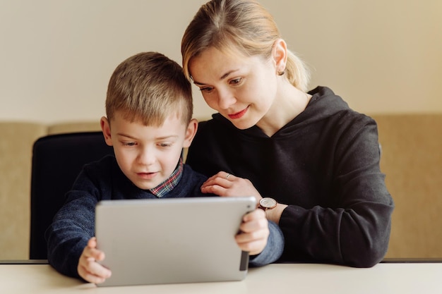 Mother using laptop and tablet teaching with her son online at home in his room