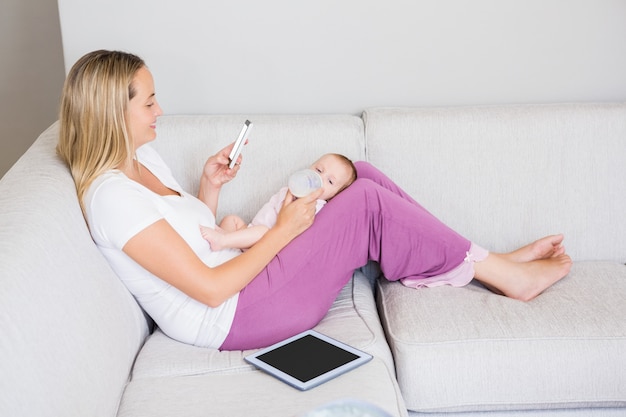 Mother using mobile phone while feeding her baby with milk bottle