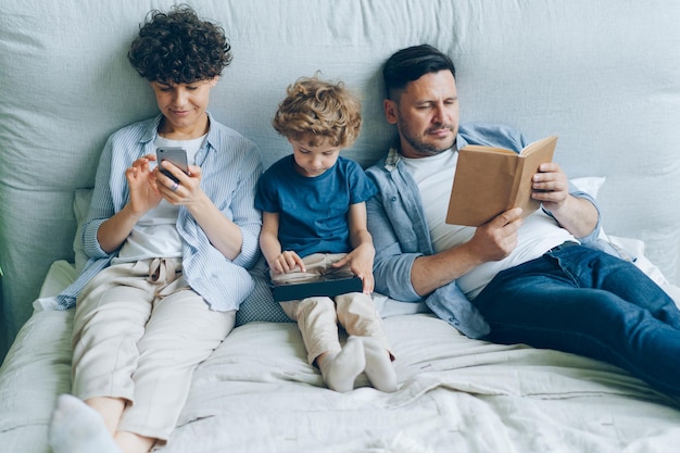 집에서 침대에서 책을 읽는 태블릿 아버지를 들고 스마트폰 아들을 사용하는 어머니